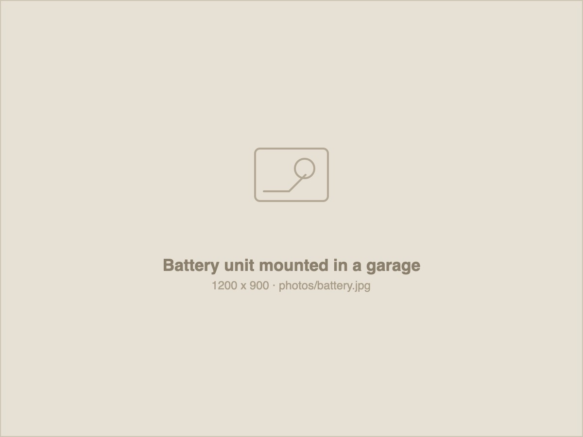 A home battery unit installed on a garage wall, wired to the switchboard.